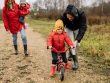 Happy family walking outdoors in fall, teaching child to ride bike.