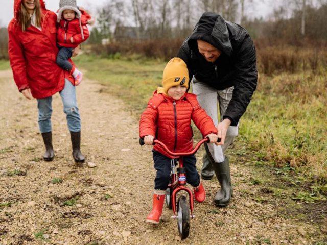 Happy family walking outdoors in fall, teaching child to ride bike.