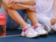 Crop anonymous female friends in activewear sitting on sports ground after training near bottle with water in daytime
